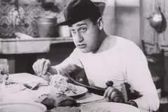 Czarno-białe ujęcie z filmu: Alberto Sordi w czapce z daszkiem nawija spaghetti na widelec i patrzy prosto w obiektyw