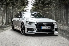 Białe Audi A6 Avant C8 stoi na szutrowej drodze w ciemnym lesie iglastym