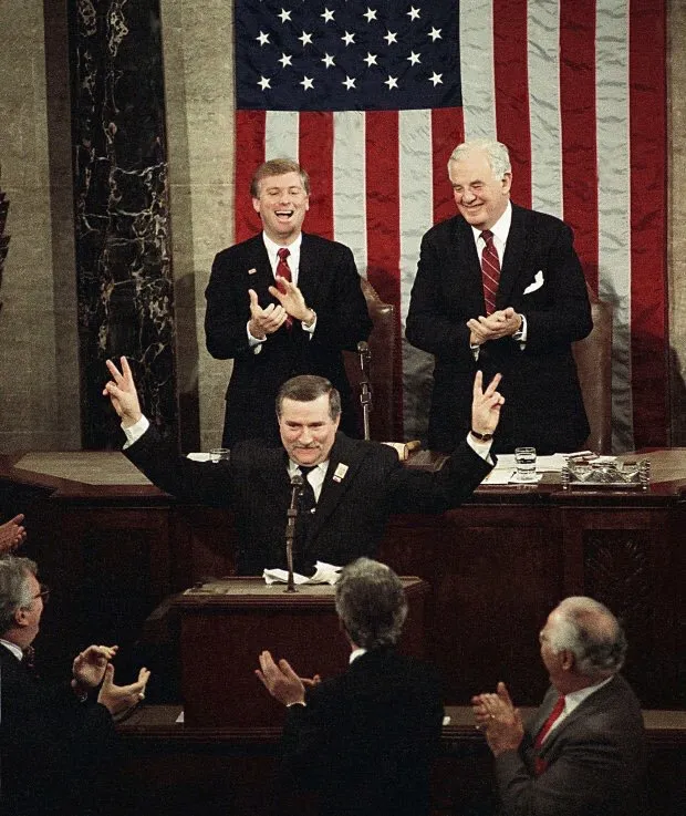 Lech Wałęsa z uniesionymi rękami pokazuje znak zwycięstwa przy mównicy Kongresu USA, za nim na tle amerykańskiej flagi klaszczą wiceprezydent Dan Quayle i spiker Izby Reprezentantów Tom Foley
