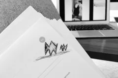 Plik wydrukowanych CV z rysunkiem długopisem na pierwszej stronie, w tle laptop z otwartym profilem kandydatki w serwisie społecznościowym