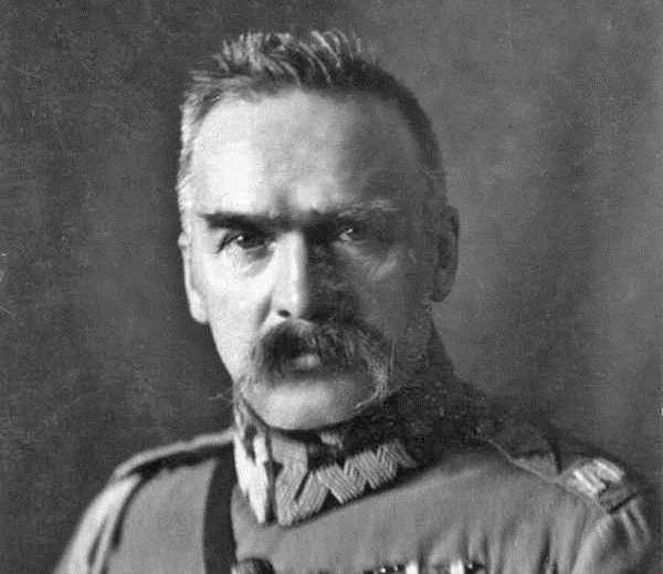 Czarno-biały portret Józefa Piłsudskiego w mundurze, z charakterystycznymi sumiastymi wąsami i krzaczastymi brwiami